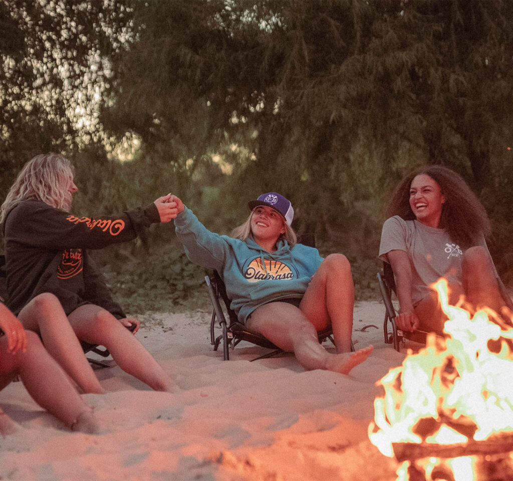 Group of friends around campfire laughing and wearing Olabrasa OG Hoodies