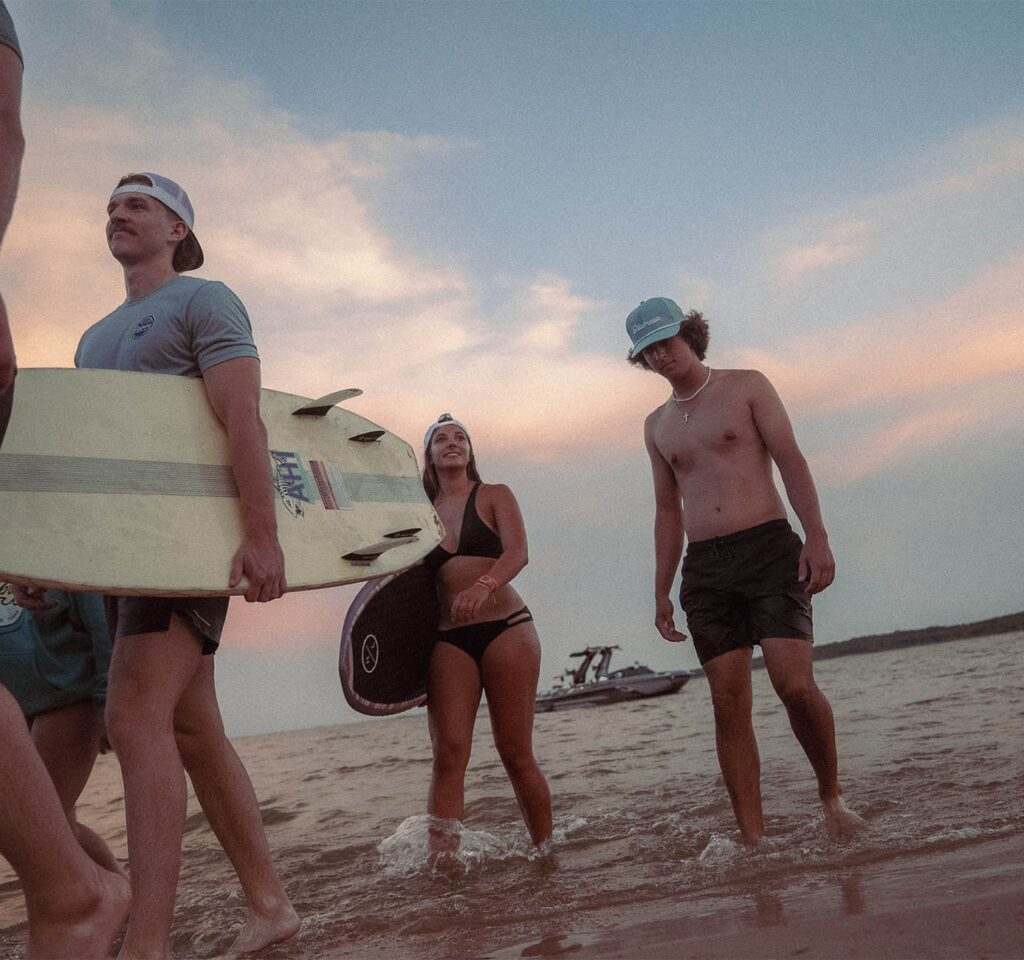 Surfers walking on beach at sunset wearing Olabrasa merch.