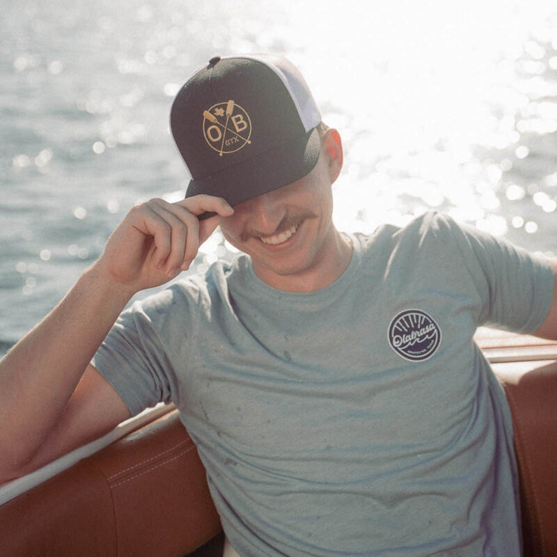 Man enjoying a sunny boat ride wearing Olabrasa OG T-Shirt and Olabrasa Paddle Flat SnapBack hat