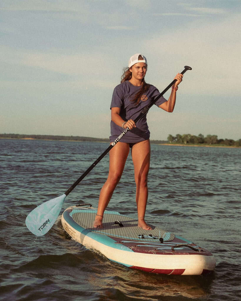Young woman wearing Olabrasa OG T-Shirt paddleboarding on calm water.