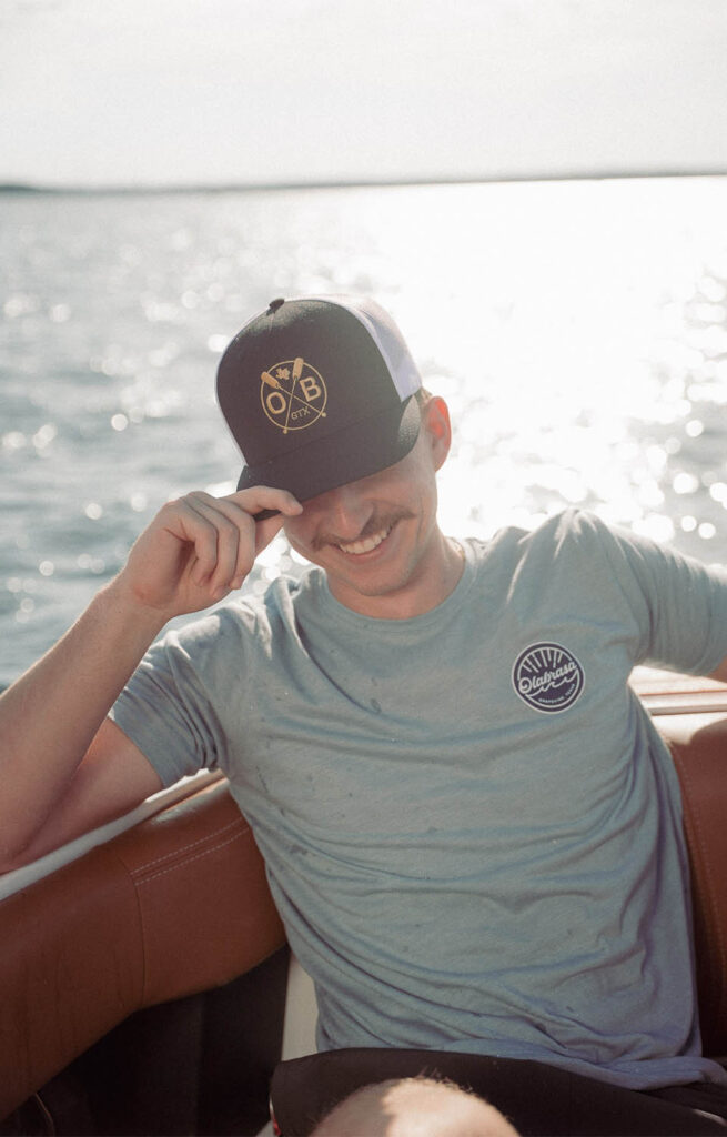 Young man wearing Olabrasa OG T-Shirt and Paddle Curved SnapBack Hat relaxing on a boat.